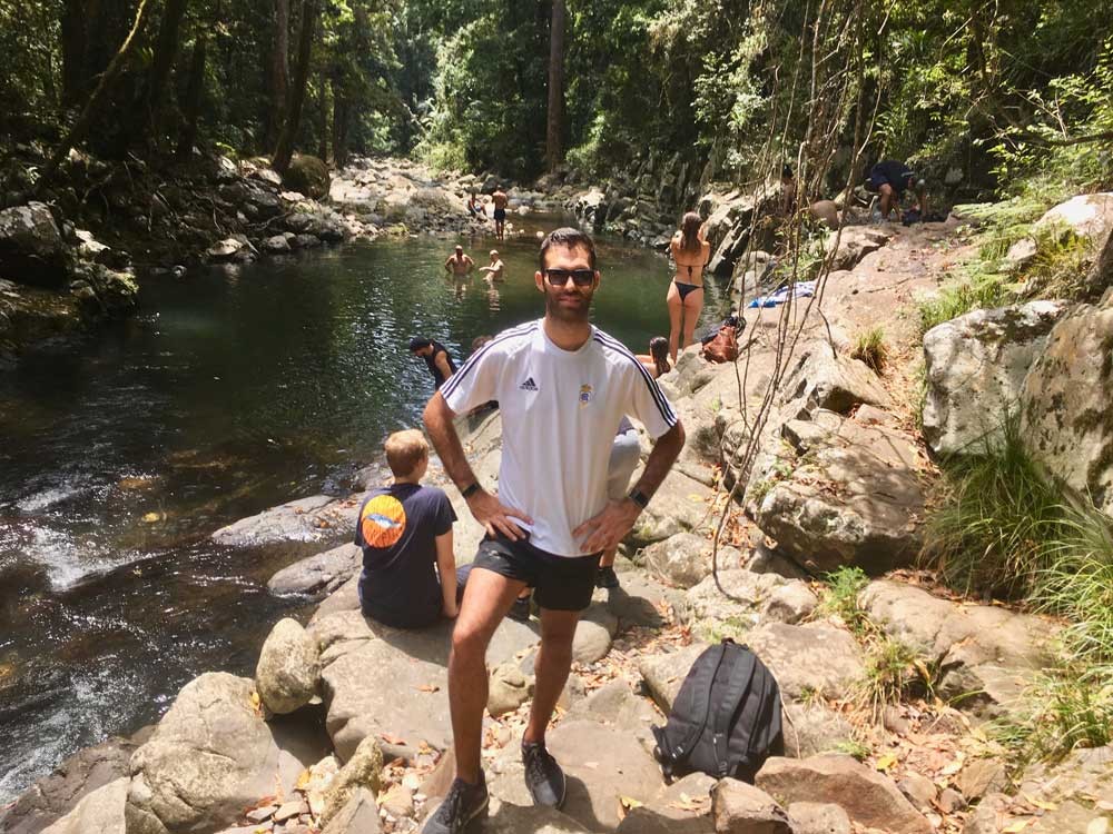 chico moreno posando y detrás rocas y un lago